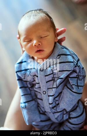 Un ragazzino stanco che dorme con gli occhi chiusi mentre sua madre lo tiene in mano a casa. Foto Stock