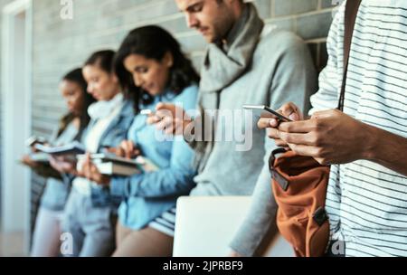 Un gruppo di studenti universitari che utilizzano il proprio cellulare mentre si trovano in un corridoio del campus. Foto Stock