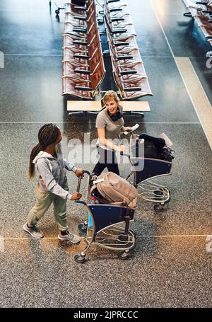 Si recava al check-in dei bagagli. Scatto ad angolo alto di due giovani donne attraenti che camminano attraverso un aeroporto. Foto Stock