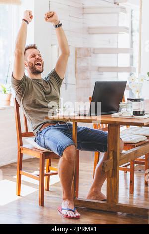 Una foto verticale di un felice uomo serbo che lavora da casa con il suo computer portatile Foto Stock