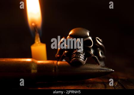 Anello d'argento con cranio e proiettile sullo sfondo di una fiamma di  candela al buio, morte e paura e guerra, armi e gotico Foto stock - Alamy