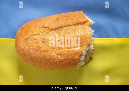 Una pagnotta di pane spezzato sullo sfondo della bandiera nazionale dell'Ucraina primo piano giallo-blu Foto Stock