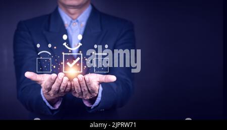 Concetto di valutazione del servizio clienti. Il maschio asiatico sorridente sta usando uno smartphone e sta premendo il sorriso del simbolo del volto in soddisfazione sul touch virtuale sc Foto Stock