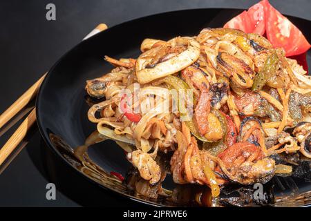 Udon tagliatelle con carne, funghi e verdure. Cosparso di semi di sesamo. Cibo asiatico, arrosto su sfondo nero, spazio copia Foto Stock