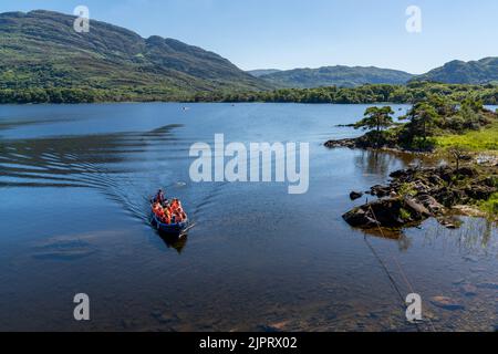 Muckross, Irlanda - 10 agosto, 2022: I turisti si godono un giro in barca sul lago Muckross nel Parco Nazionale di Killarney in una bella giornata estiva Foto Stock