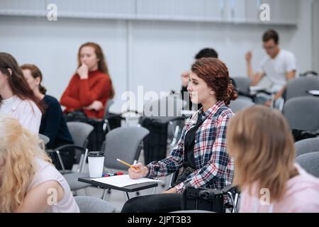 Diversi studenti universitari in abiti casual sono seduti al pubblico per una lezione e l'ascolto dell'insegnante. Foto Stock