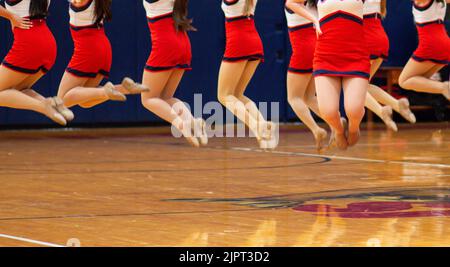 Ballerini kickline di scuola superiore in aria mentre si esibiscono a metà tempo di una partita di basket Foto Stock