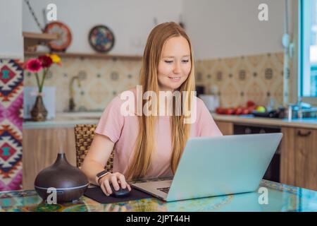 Diffusore di olio essenziale sul tavolo che fuma mentre la donna usa un computer portatile Foto Stock