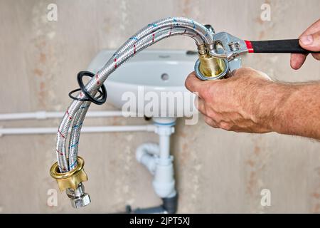 Lavori idraulici per sostituire il rubinetto dell'acqua nel bagno, l'idraulico fissa il tubo di collegamento intrecciato sul rubinetto. Foto Stock