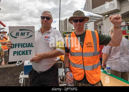 Southend on Sea, Regno Unito. 20 agosto 2022. I membri dell'Unione nazionale dei lavoratori ferroviari, marittimi e dei trasporti (RMT) partecipano a una protesta ufficiale per picchetti. Uno ha un cartello con la scritta "RMT OFFICIAL PICKET" e indossa una camicia bianca con un cinturino giallo. L'altro solleva un pugno stringato in solidarietà, indossando un gilet arancione ad alta visibilità contrassegnato "RMT UNION". Lavoratori della RMT e personale ferroviario su una linea di picchetti fuori dalla stazione di Southend Victoria mentre la controversia in corso con Network Rail continua. Penelope Barritt/Alamy Live News Foto Stock