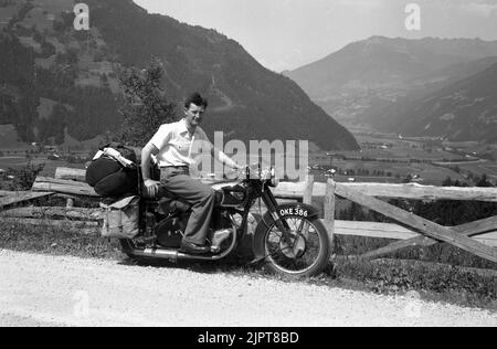 1950s, storico, su una strada di ghiaia di montagna, in una vacanza in giro per l'Europa, un giovane seduto su una moto BSA dell'epoca, bagagli e panniere in tela sul retro della moto. Foto Stock