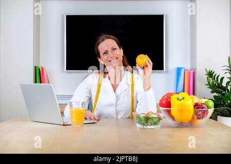 Ritratto di nutrizionista sorridente che tiene un arancione. Donna dietetica con un grande sorriso e mostrando all'arancione. Vitamine e concetto di dieta sana Foto Stock