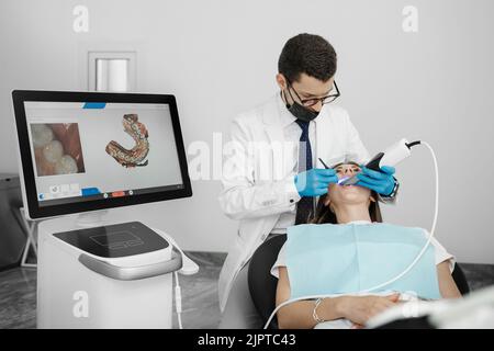 Paziente di lavaggio ortodontista maschile con scanner dentario intraorale e controlli processo sullo schermo. Concetto di protesi e stomatologia. Foto Stock