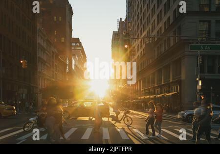 Persone, biciclette e taxi in un vivace incrocio sulla 5th Avenue a New York City con la luce del tramonto che splende sullo sfondo Foto Stock