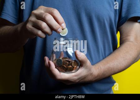 un uomo salva raccogliendo monete in un vaso di vetro Foto Stock