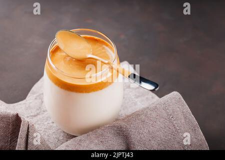 Caffè Dalgona fatto in casa su sfondo scuro. Dalgona caffè schiumoso con un cucchiaio su un tovagliolo di lino. Bevanda sudcoreana con caffè istantaneo montato, su Foto Stock