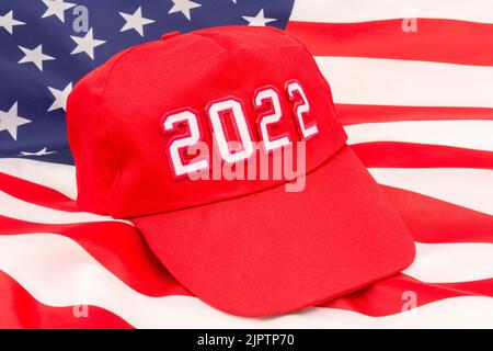 Cappello rosso TIPO MAGA con 2022 sullo sfondo Bandiera delle Stelle e delle strisce degli Stati Uniti. Per le vittorie repubblicane in 2022 elezioni di Midterm degli Stati Uniti in novembre e la Red Wave repubblicana. Foto Stock