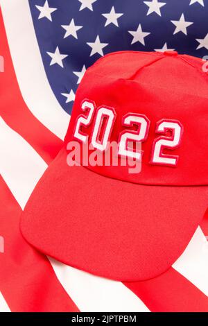 Cappello rosso TIPO MAGA con 2022 sullo sfondo Bandiera delle Stelle e delle strisce degli Stati Uniti. Per le vittorie repubblicane in 2022 elezioni di Midterm degli Stati Uniti in novembre e la Red Wave repubblicana. Foto Stock