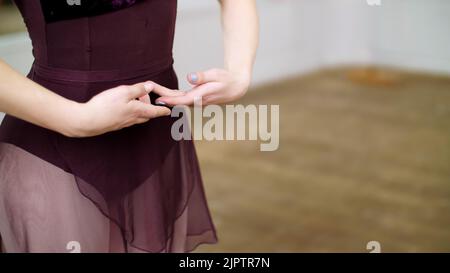 Primo piano, nella sala da ballo, la giovane ballerina in leotard viola esegue la prima posizione delle mani, elegantemente. Foto di alta qualità Foto Stock