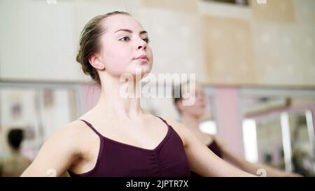 Nella sala da ballo, la giovane ballerina in leotard viola esegue un certo esercizio di balletto, prima posizione delle mani,. Foto di alta qualità Foto Stock