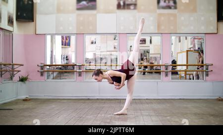 Nella sala da ballo, la giovane ballerina in leotard nera esegue una grande battaglia indietro, solleva la gamba dietro elegantemente, in classe balletto. Foto di alta qualità Foto Stock