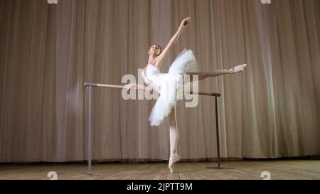 prove di balletto, nella sala del teatro antico. Giovane ballerina in gonna di balletto bianco, tutu, è impegnata a balletto, esegue elegantemente un certo esercizio di balletto, atteggiamento allonge, in piedi vicino a barre. Foto di alta qualità Foto Stock