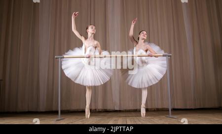 prove di balletto, nella sala del teatro antico. Ballerine giovani in gonne di balletto bianco, tutus, sono impegnati a balletto, eseguire elegantemente un certo esercizio di balletto, passare , attidude, in piedi vicino a barre. Foto di alta qualità Foto Stock