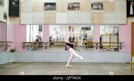 Nella sala da ballo, giovane ballerina in lotarda nera esegue pas courru , pointe , si sta muovendo attraverso la classe balletto elegantemente,. Foto di alta qualità Foto Stock