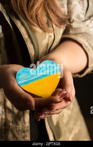 Donna militare con un cuore blu-giallo nelle sue mani. Un simbolo di amore per l'Ucraina Foto Stock