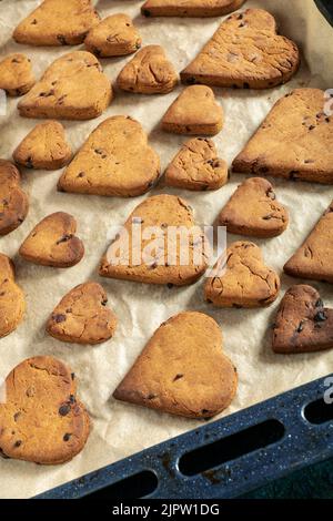 Biscotti a forma di cuore con gocce di cioccolato su un vassoio da forno Foto Stock