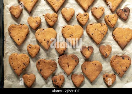 Biscotti a forma di cuore con gocce di cioccolato su un vassoio da forno Foto Stock