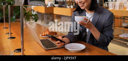 Giovane donna asiatica d'affari vestito bere caffè utilizzando il telefono nel caffè. Foto Stock