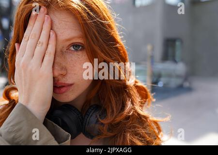 Teen redhead hipster ragazza che guarda la macchina fotografica in piedi su sfondo urbano. Foto Stock