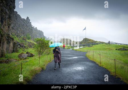 Una donna che cammina con l'ombrello lungo un sentiero in una giornata di pioggia nel Parco Nazionale di Thingvellir in Islanda Foto Stock