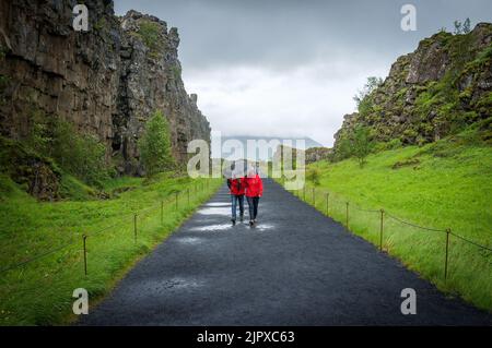 Una gente che cammina con gli ombrelloni lungo un sentiero in una giornata di pioggia nel Parco Nazionale di Thingvellir in Islanda Foto Stock