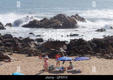 Famiglia godendo di una giornata sulla spiaggia di Foz do Douro nella zona di Porto in Portogallo. Le onde si schiantano sulle rocce mentre la famiglia si siede e si rilassa. Foto Stock