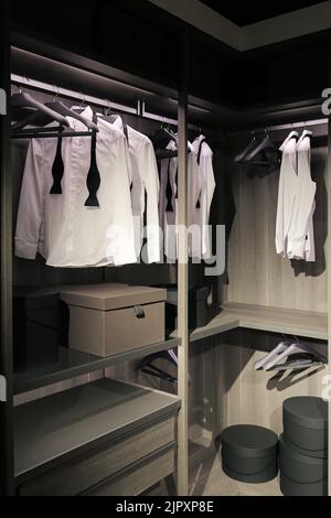Eleganti camicie bianche appese ad appendiabiti nell'armadio Foto Stock