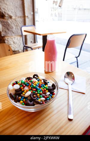 Colazione a secco in ciotola di vetro su un tavolo di legno nel caffè. Deliziosi cornflakes e latte rosa in una bottiglia. Colazione sana e utile. Cibo per Foto Stock