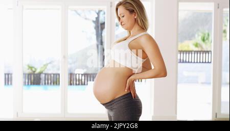 Avere una schiena forte è un grande Plus durante la gravidanza. Ritratto corto di una giovane donna incinta attraente in piedi con le mani sulla schiena. Foto Stock