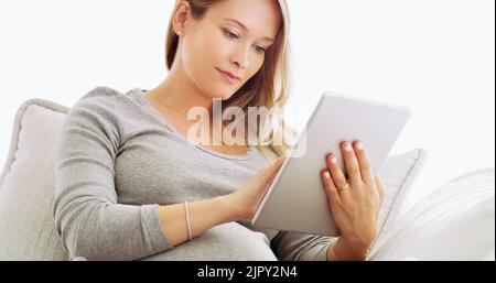 Può fare tutto dalla comodità della sua casa. Una donna incinta che usa un tablet a casa. Foto Stock