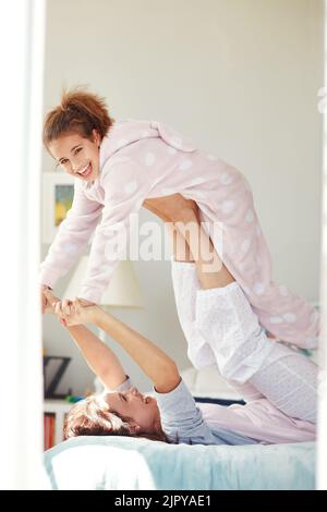 Il divertimento si ferma quando le luci si spengo. Una giovane madre che solleva la figlia con le gambe mentre si sdraia sul letto. Foto Stock