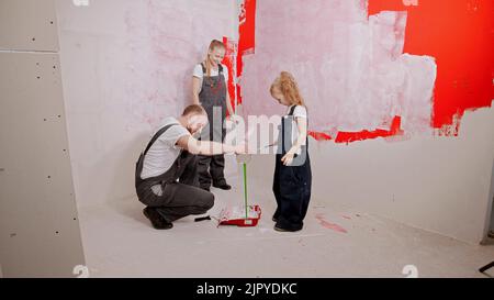 Mamma e figlia stanno guardando come il padre sta versando vernice verde nel vassoio Foto Stock