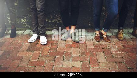 Tutti abbiamo il nostro paio di scarpe preferito, un gruppo di persone diverse che si levano in piedi insieme su un marciapiede pavimentato. Foto Stock