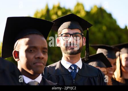 Alla chiusura di un capitolo, si apre un altro capitolo. Ritratto di uno studente universitario in piedi tra i suoi compagni di classe il giorno della laurea. Foto Stock