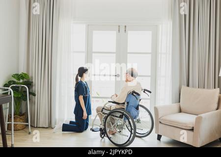 L'uomo asiatico anziano in sedia a rotelle riceve assistenza medica per lesioni, prendersi cura e prendere a guardare fuori dalla finestra Foto Stock