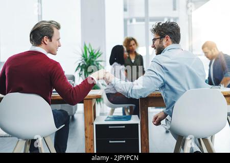 Sosterranno il successo degli altri due giovani colleghi che si danno un pugno alle loro scrivanie in un ufficio moderno. Foto Stock
