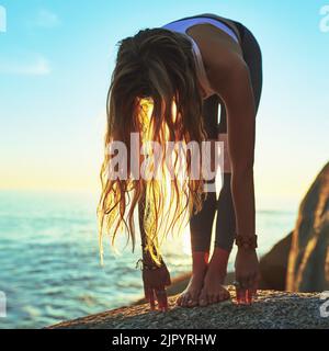 Lasciatevi andare. Una giovane atletica che pratica yoga sulla spiaggia. Foto Stock