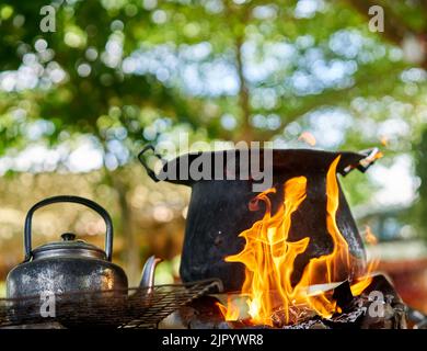 Una grande pentola nera e un vecchio bollitore su un fuoco all'aperto. Foto Stock