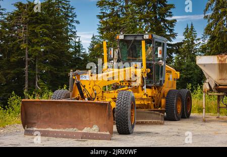 Motorgrader per la costruzione di strade in aree forestali. Greyder livella la sabbia, il terreno e la ghiaia. Macchinari pesanti e attrezzature da costruzione per il livellamento Foto Stock