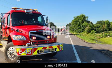 Un camion antincendio rosso con un elicottero di salvataggio dietro di esso su una strada circondata da un'area verde Foto Stock